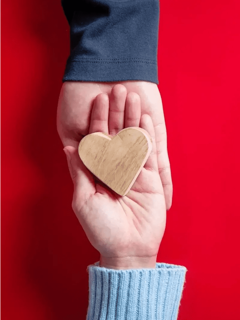 Cuore in legno tenuto in due mani su sfondo rosso – simbolo di solidarietà e impegno sociale di Bongiovi