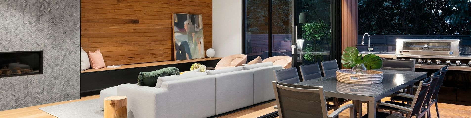 Moderno soggiorno e zona pranzo open space con dettagli in legno, camino elegante e area barbecue esterna.