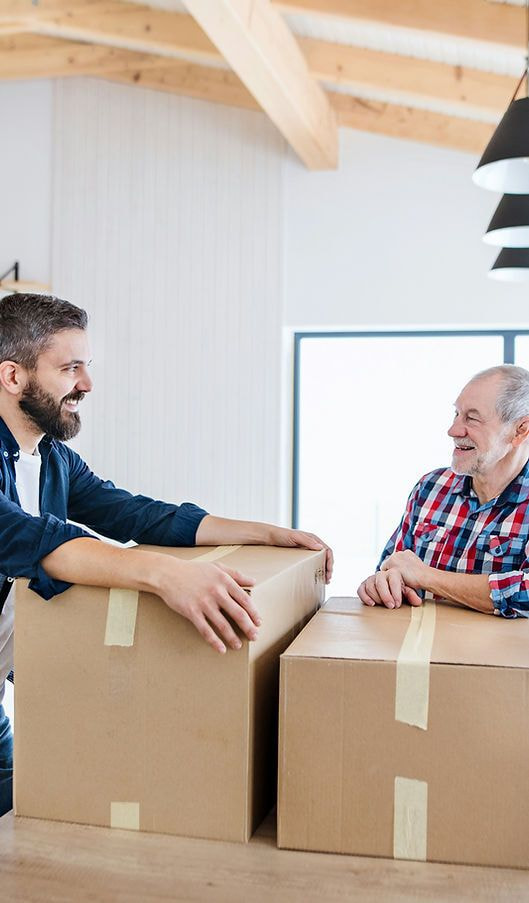 Vater und Sohn packen gemeinsam Umzugskartons in einem gemütlichen Zuhause aus.