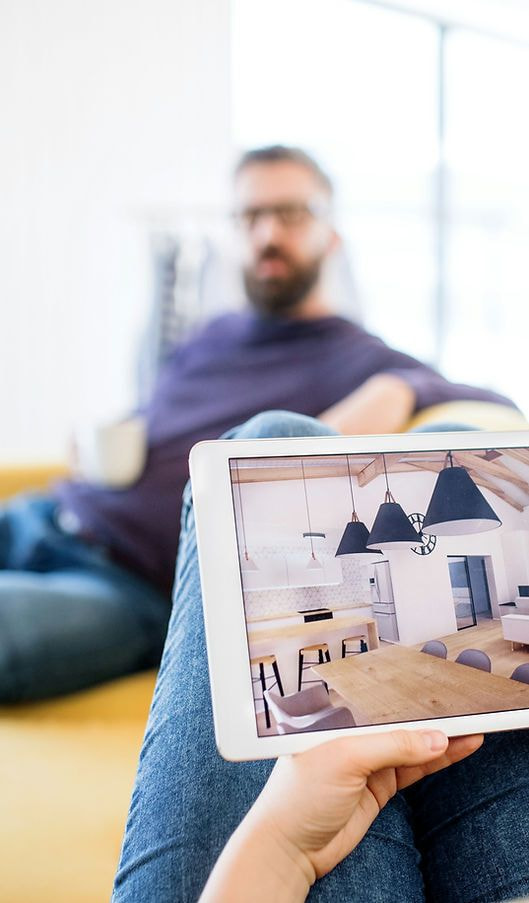Smarthome-Tablet steuert die Küche, während ein Mann entspannt auf dem Sofa sitzt.