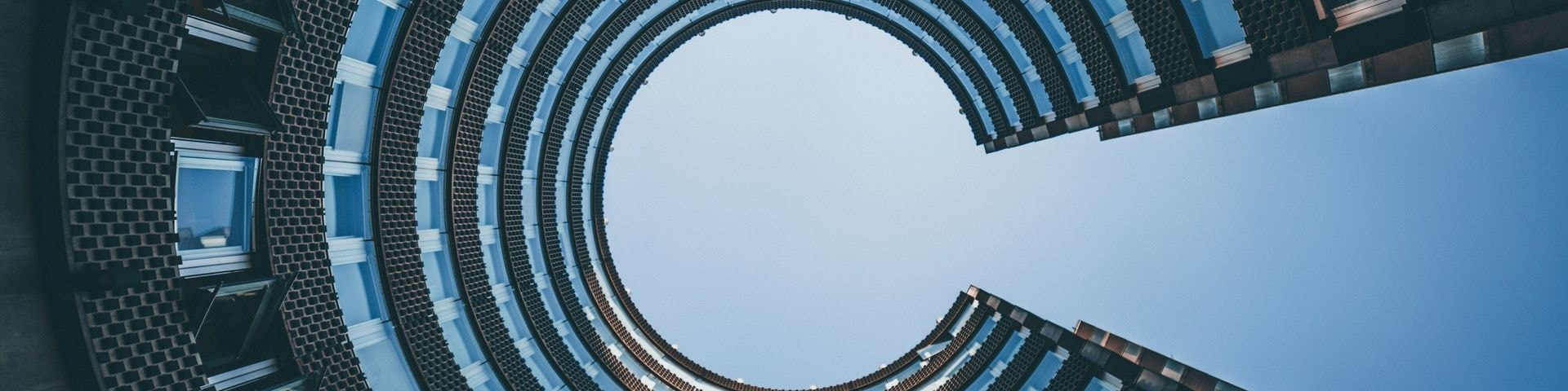 Modern circular building with a futuristic design, captured from a low-angle perspective against a clear blue sky. Modern circular building with a futuristic design, captured from a low-angle perspective against a clear blue sky.